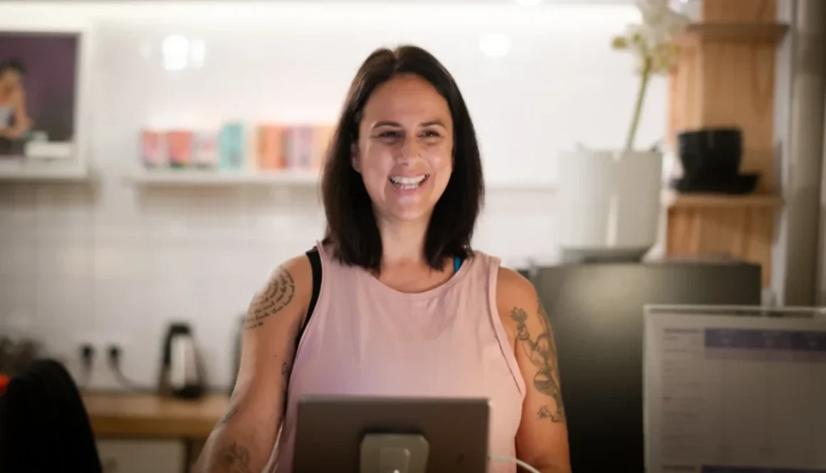 Eine Frau lächelt vor einem Computerbildschirm im Yogastudio, bereit für eine Schnupper-Yogastunde.