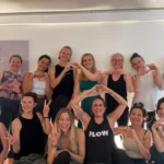 Eine Gruppe von Absolventinnen der Yogalehrerausbildung formt mit den Händen Herzen und lächelt fröhlich in die Kamera.
