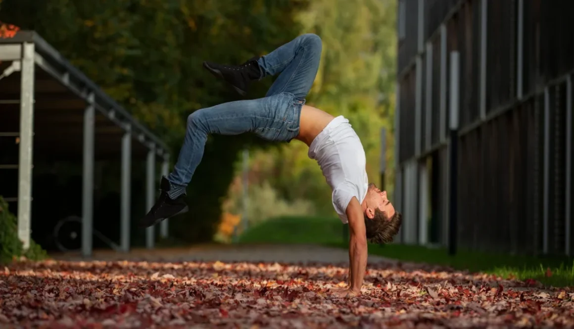 Ein Mann macht einen Handstand auf bunten Herbstblättern in einem Park.