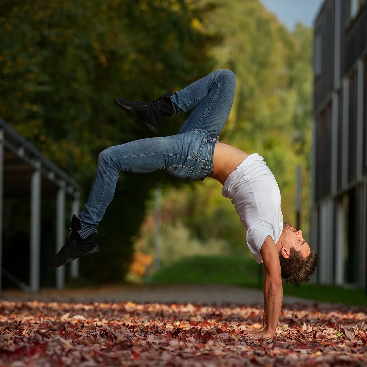 Ein Mann macht einen Handstand auf bunten Herbstblättern in einem Park.