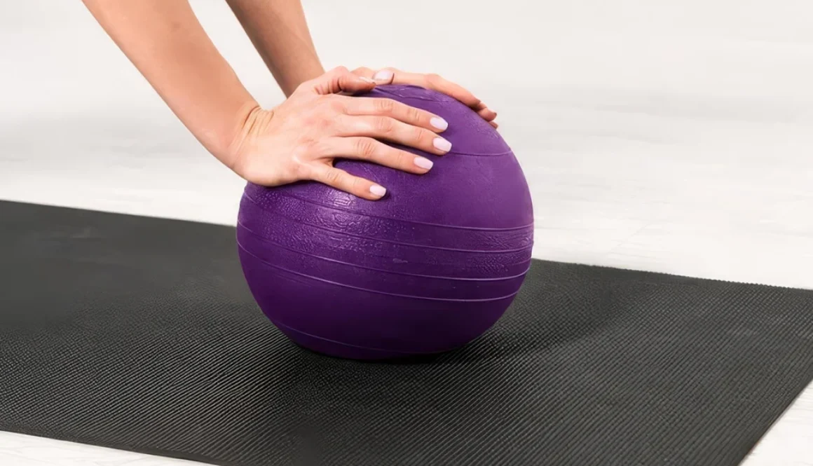 Eine Hand liegt auf einem lila Pilates-Mobile, das auf einer Matte in einem hellen Raum platziert ist.