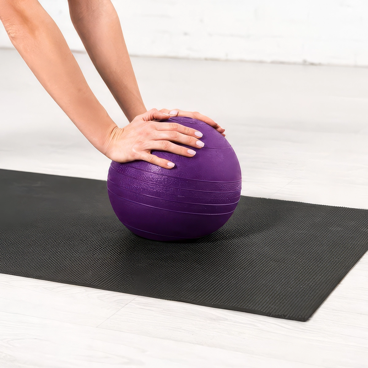 Eine Hand liegt auf einem lila Pilates-Mobile, das auf einer Matte in einem hellen Raum platziert ist.