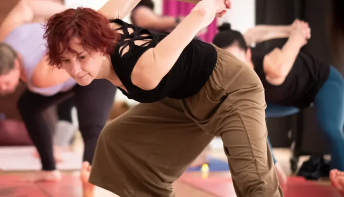Eine Frau praktiziert Yoga in einer Gruppe, während sie sich in eine herausfordernde Pose beugt.