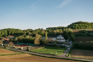 Eine idyllische Landschaft mit dem Hotel Albizia inmitten von Feldern und Bäumen bei klarem Himmel.