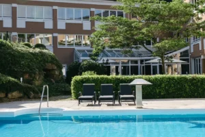 Ein sonniger Tag im Garten des Hotel Albizia mit einem einladenden Pool und gemütlichen Liegestühlen lädt zum Entspannen ein.