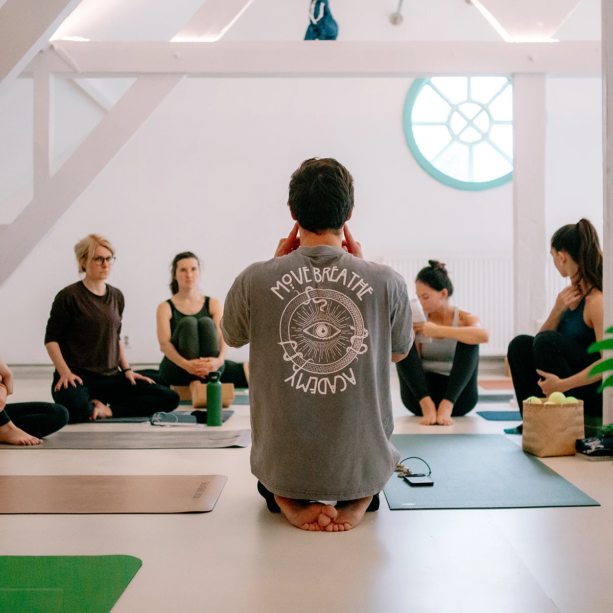 Eine Gruppe von Yogalehrer:innen sitzt aufmerksam im Kreis, während ein Lehrer Anweisungen gibt.