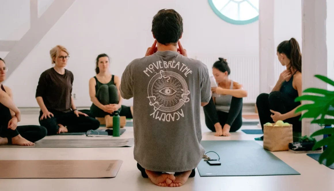 Eine Gruppe von Yogalehrer:innen sitzt aufmerksam im Kreis, während ein Lehrer Anweisungen gibt.