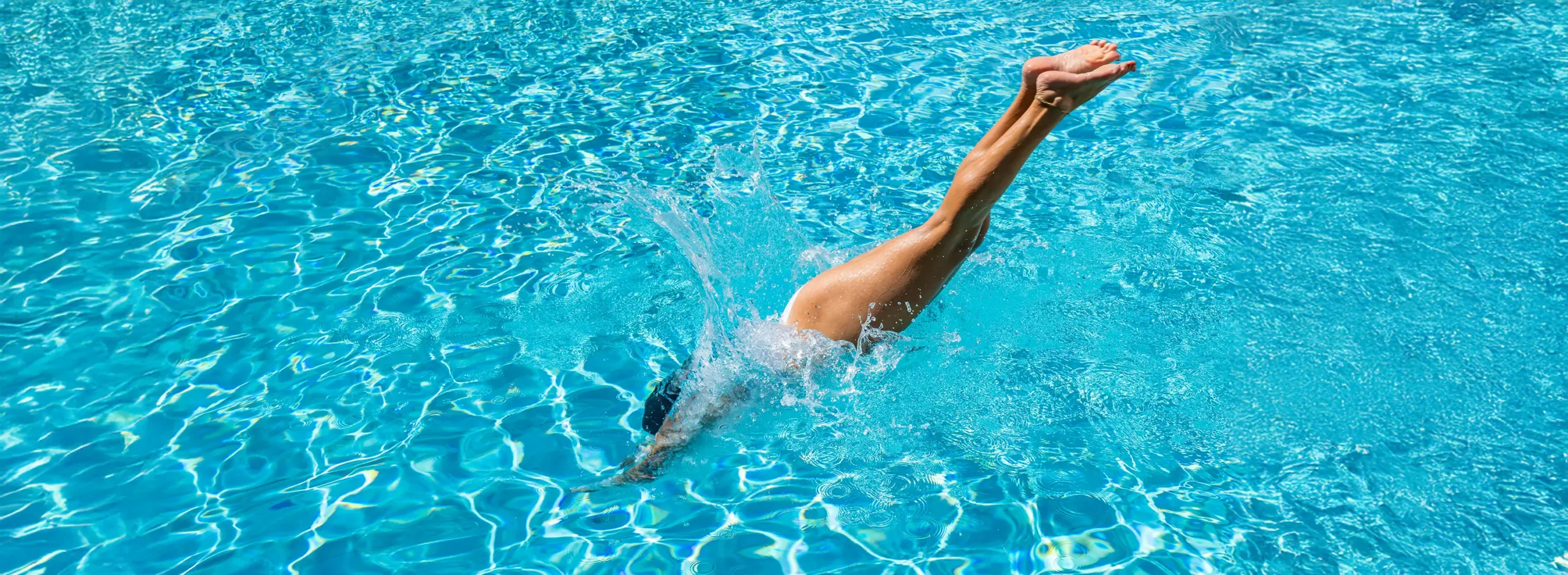 Eine Frau taucht kopfüber in einen klaren, blauen Pool ein, was an ein erfrischendes Sommerretreat erinnert.