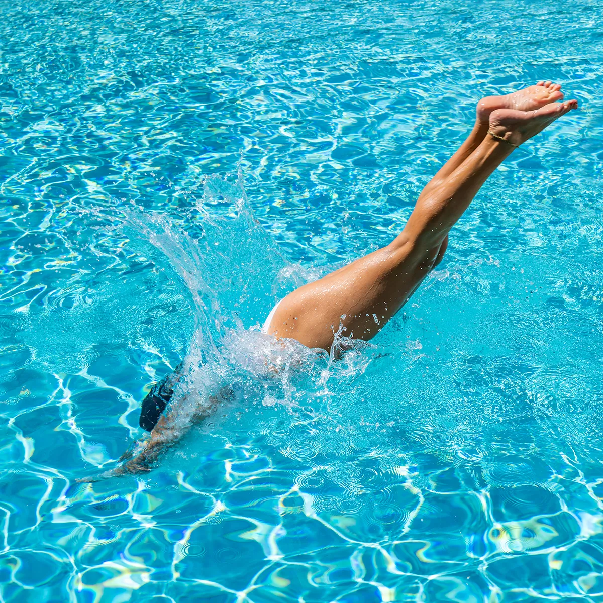 Eine Frau taucht kopfüber in einen klaren, blauen Pool ein, was an ein erfrischendes Sommerretreat erinnert.