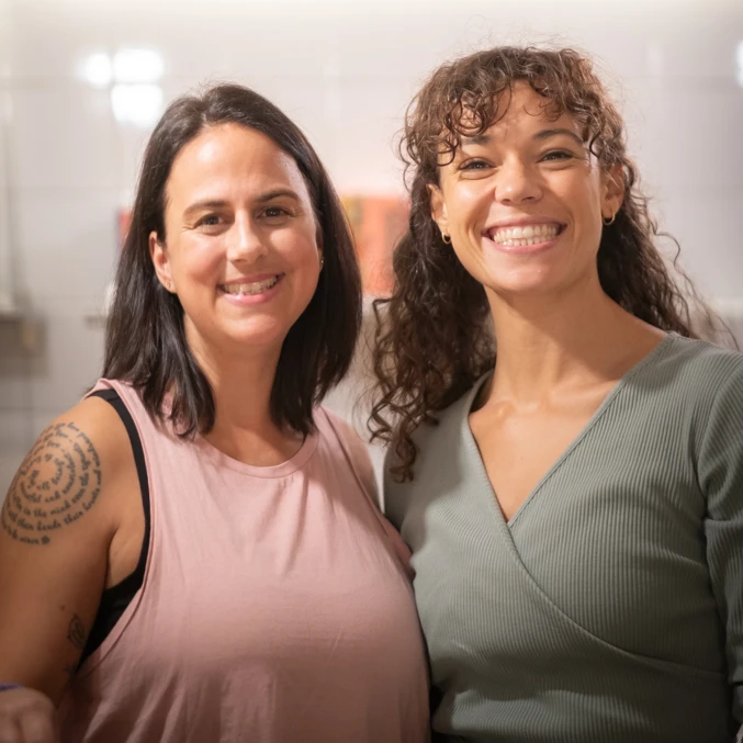 Zwei Frauen lächeln in die Kamera und strahlen positive Energie aus, passend zum Yogastudio.