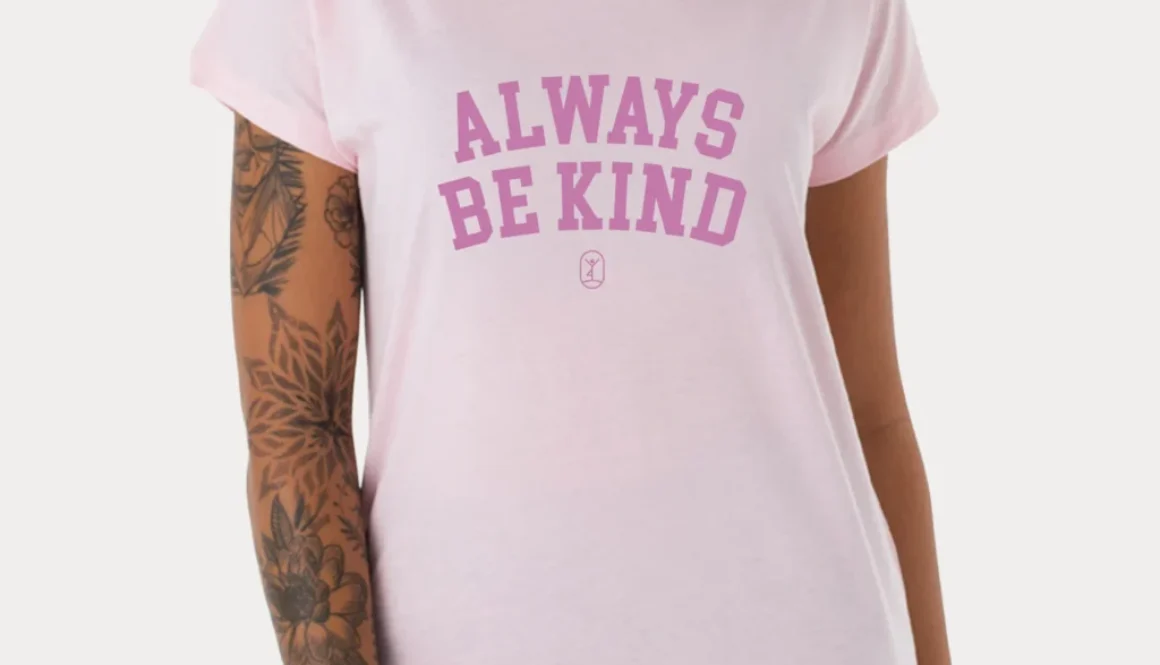 Eine Frau trägt ein rosa Shirt mit dem Schriftzug "Always Be Kind" und strahlt positive Energie aus.