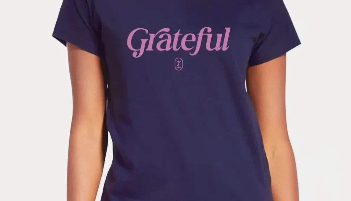 Eine Person trägt ein navyfarbenes Shirt mit dem Schriftzug "Grateful" und lächelt zufrieden in die Kamera.