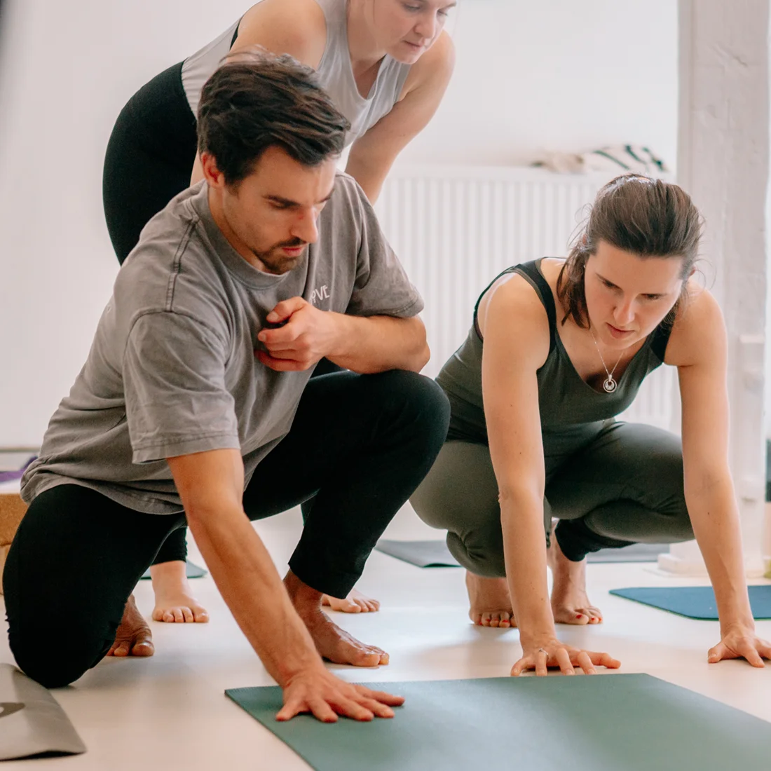 Drei Yogalehrer unterstützen Teilnehmer in einer Klasse bei Nils, während sie auf ihre Matten vorbereiten.