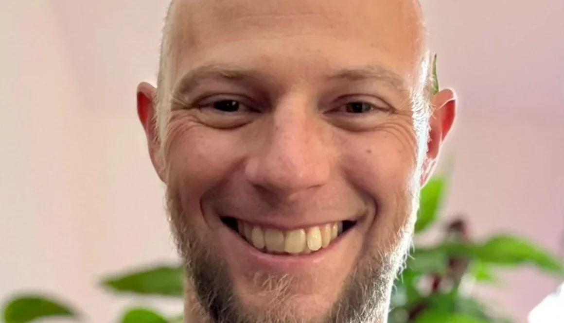 Marko lächelt freundlich vor einer grünen Pflanzenkulisse in einem hellen Raum des YOGALIFE-Studios.