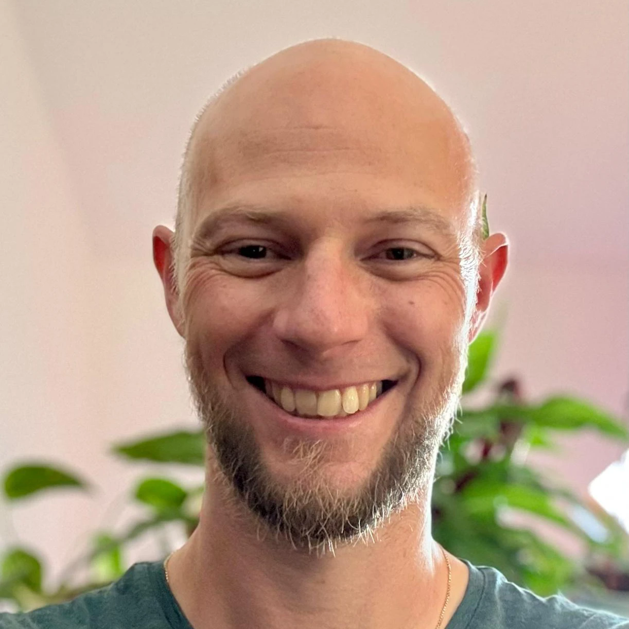 Marko lächelt freundlich vor einer grünen Pflanzenkulisse in einem hellen Raum des YOGALIFE-Studios.